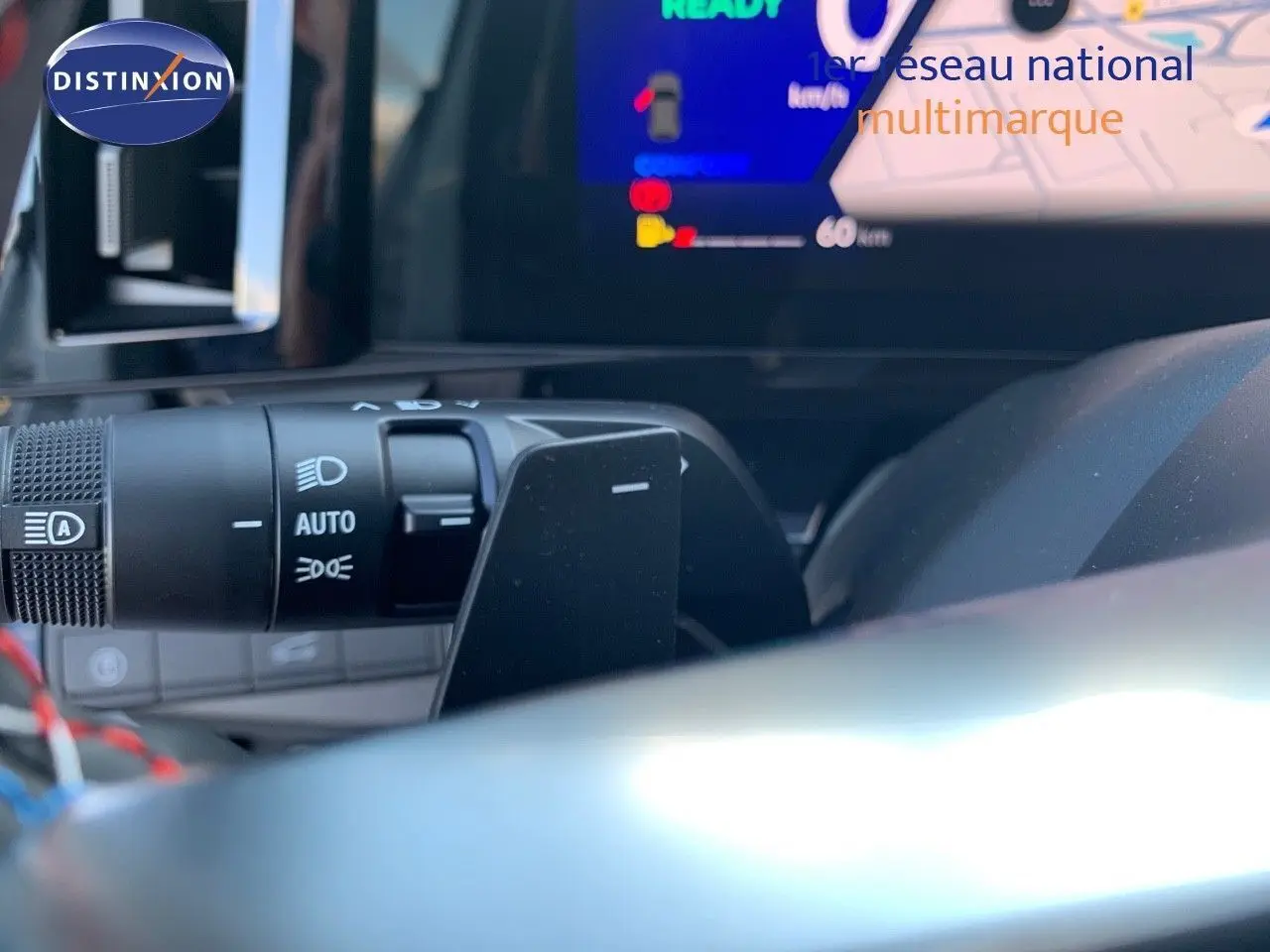 Gros plan sur la commande des phares et le volant d'un Renault Austral 2024 hybride avec tableau de bord numérique allumé.