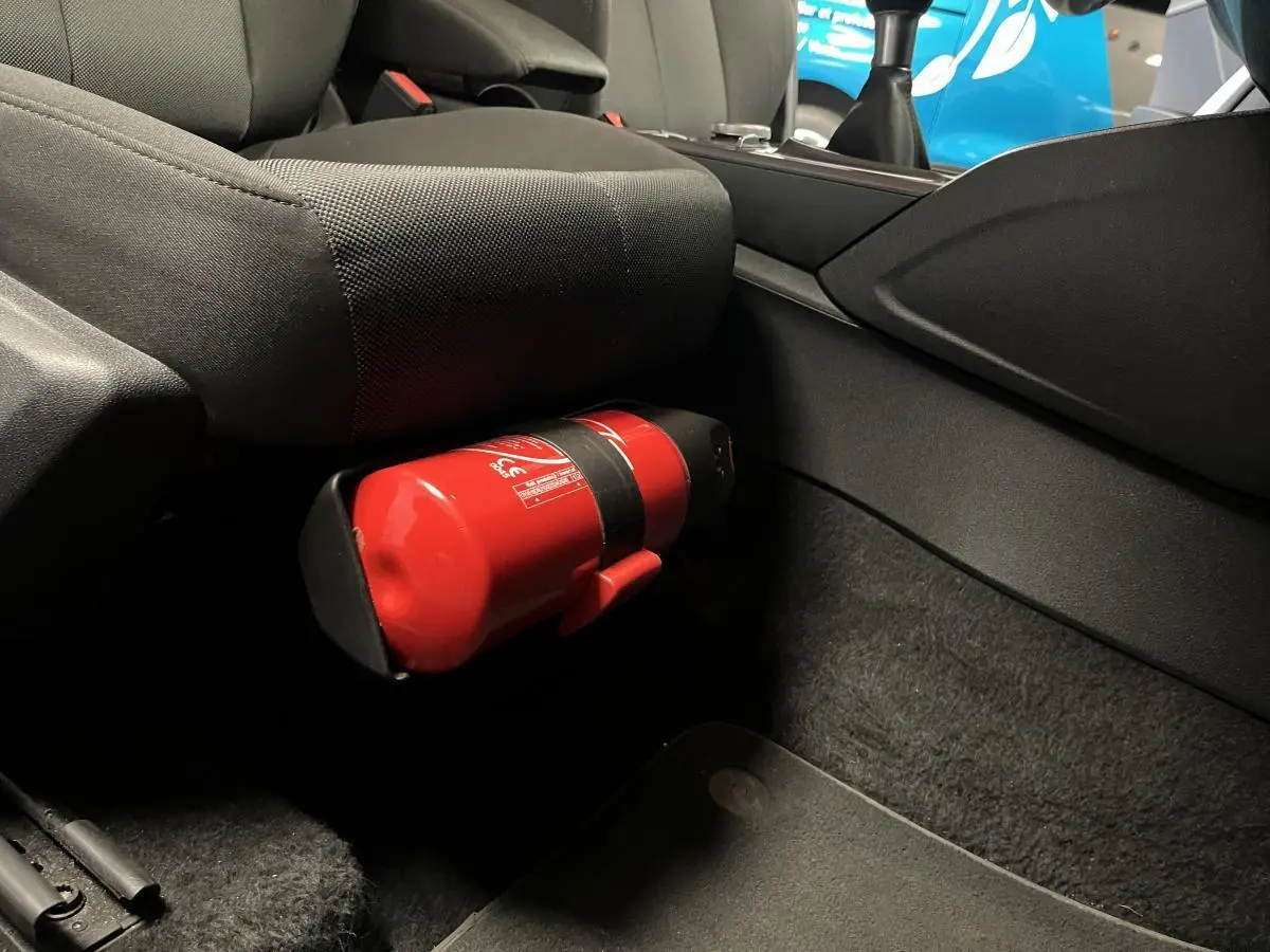 Gros plan sur l'extincteur rouge fixé sous le siège avant côté passager d'un Audi Q2 Business line gris.