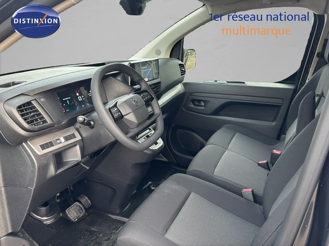Vue intérieure côté conducteur du Citroën Jumpy Fourgon gris titane, montrant le tableau de bord et les sièges noirs.
