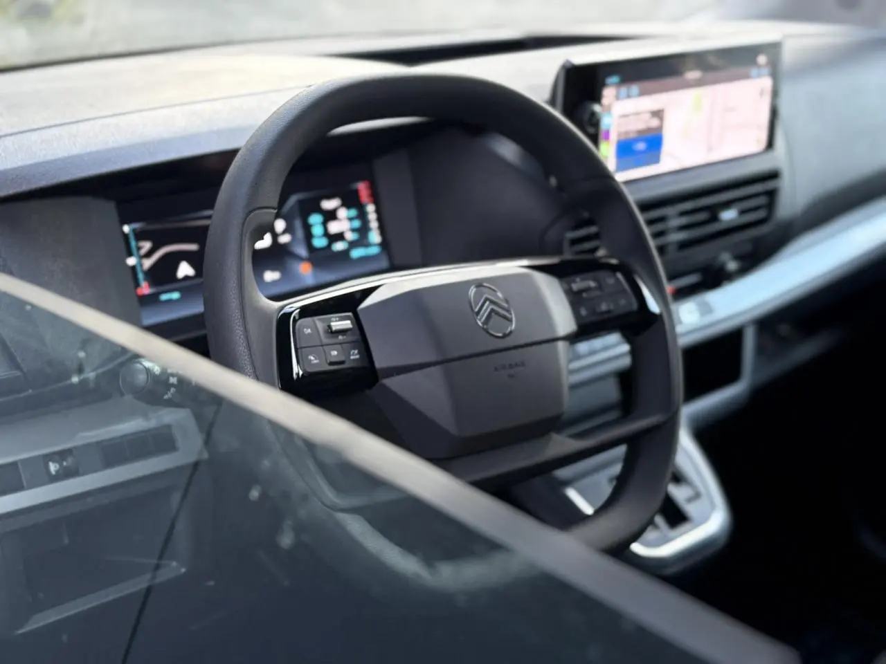 Vue rapprochée du volant Citroën Jumpy 2025 avec commandes intégrées et écran GPS tactile en arrière-plan.