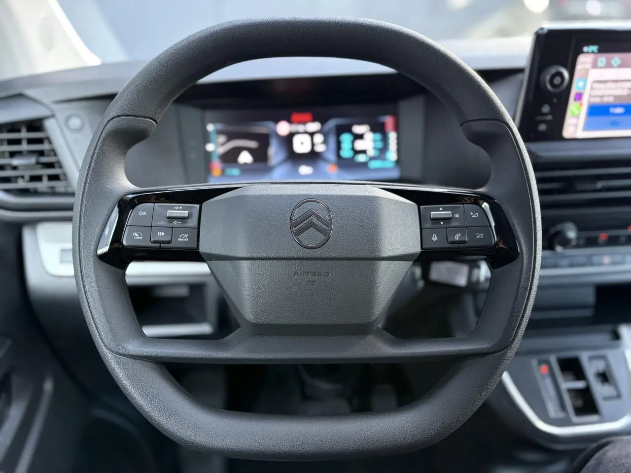 Vue rapprochée du volant noir du Citroën Jumpy XL 2025 avec commandes intégrées et tableau de bord numérique flou.