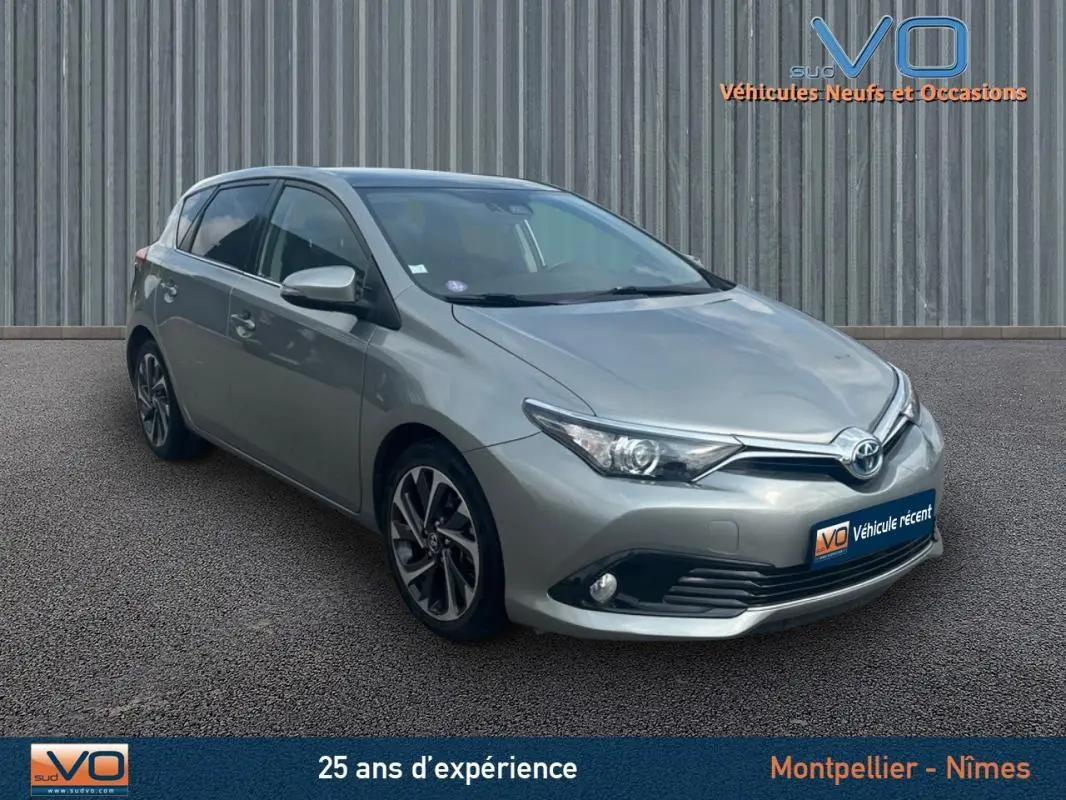 Vue 3/4 avant d'une Toyota Auris Business Hybride gris clair avec jantes alliage 17 pouces sur sol gris.