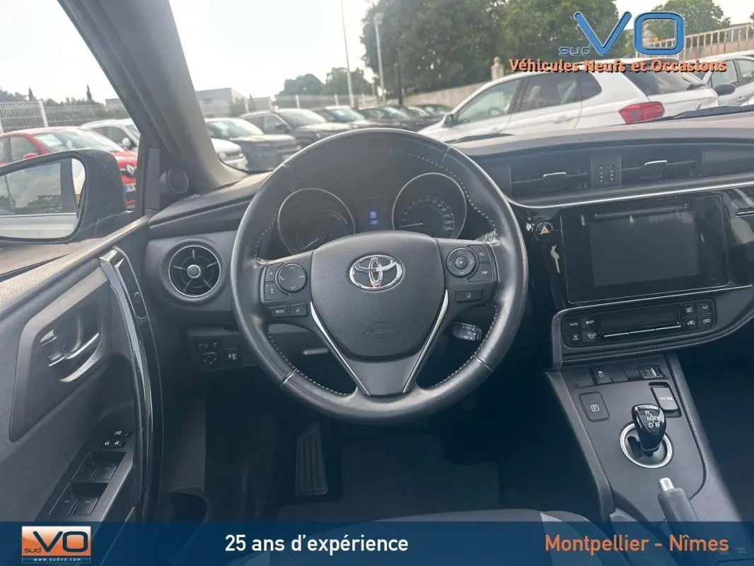 Vue intérieure du poste de conduite de la Toyota Auris Business Hybride 2016, volant multifonctions et écran tactile central visibles.