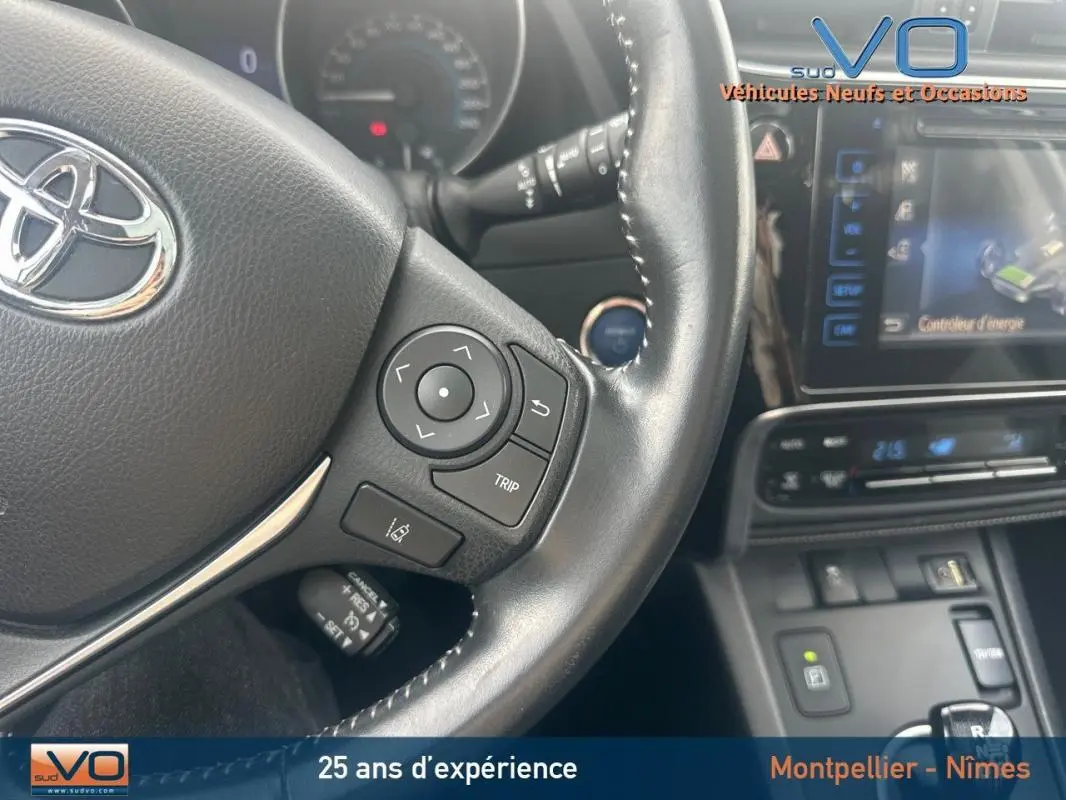 Gros plan sur le volant multifonctions en cuir noir de la Toyota Auris Business Hybride 2016 avec tableau de bord et écran tactile.