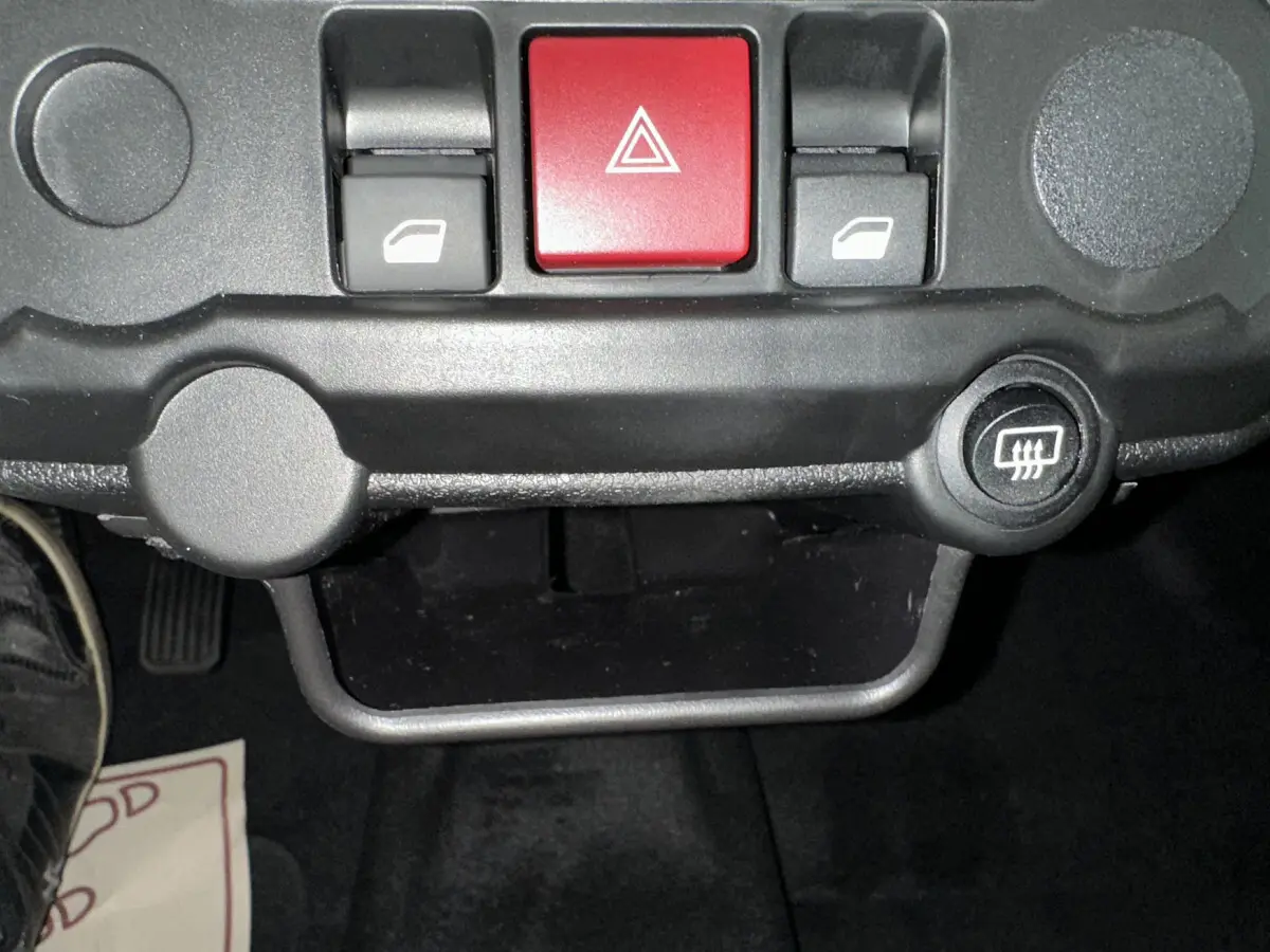 Gros plan sur les commandes centrales du tableau de bord de l'AIXAM AMBITION E CITY PACK rouge, avec bouton de warning rouge et commandes de vitres.