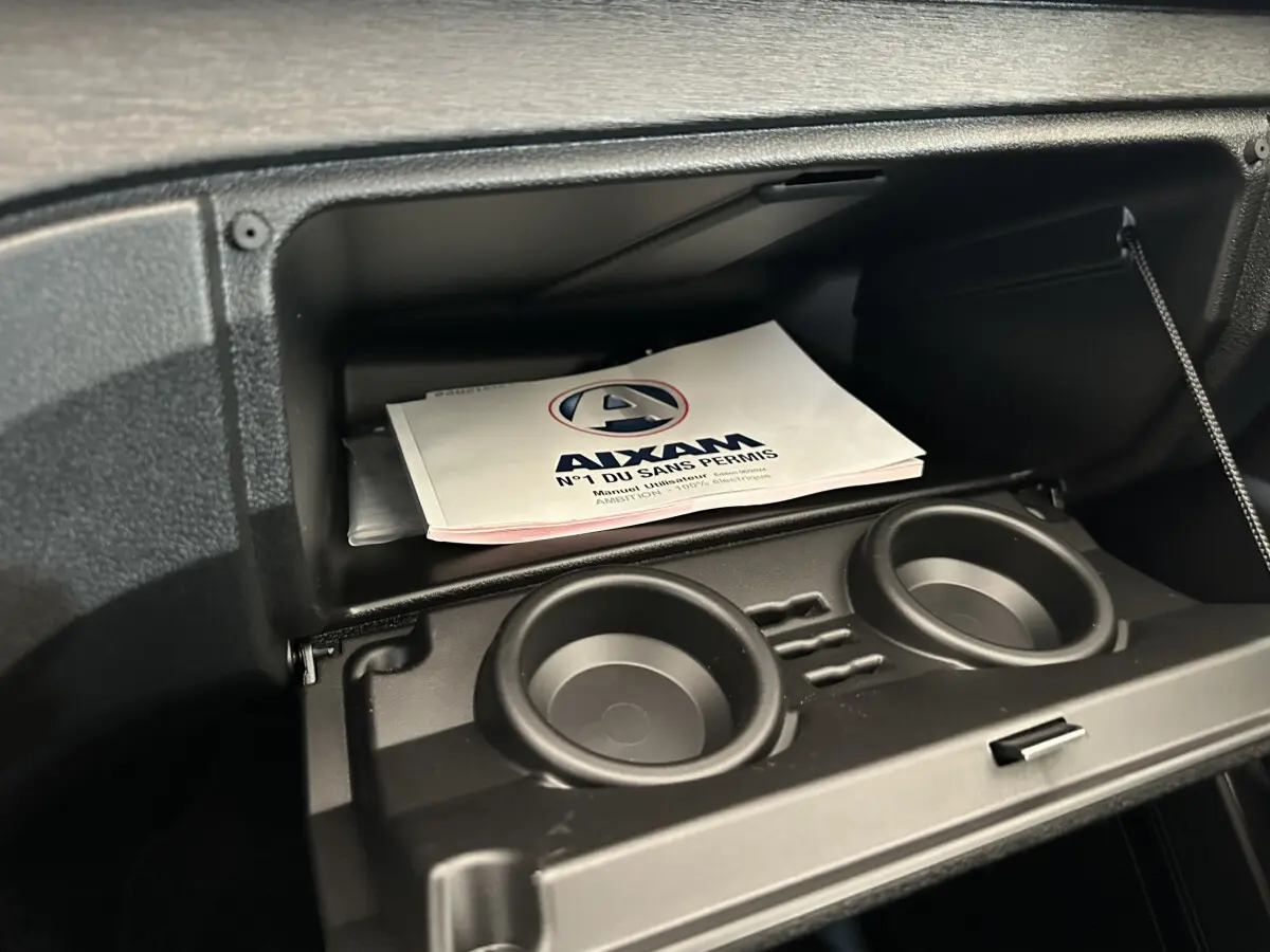 Vue rapprochée de la boîte à gants ouverte de l'AIXAM AMBITION E CITY PACK 2025 avec porte-gobelets intégrés.
