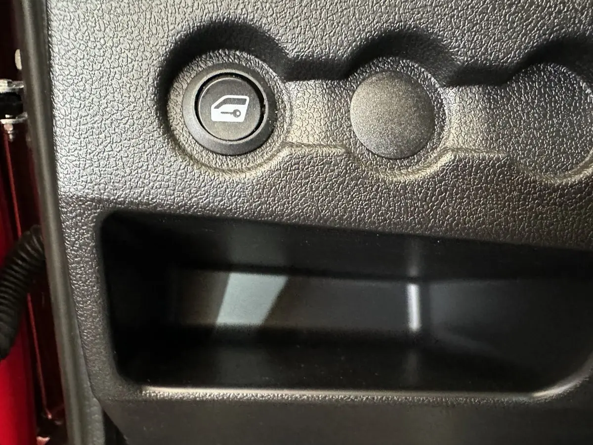 Bouton d'ouverture du coffre sur la console intérieure noire d'une Aixam Ambition E City Pack rouge, côté conducteur.