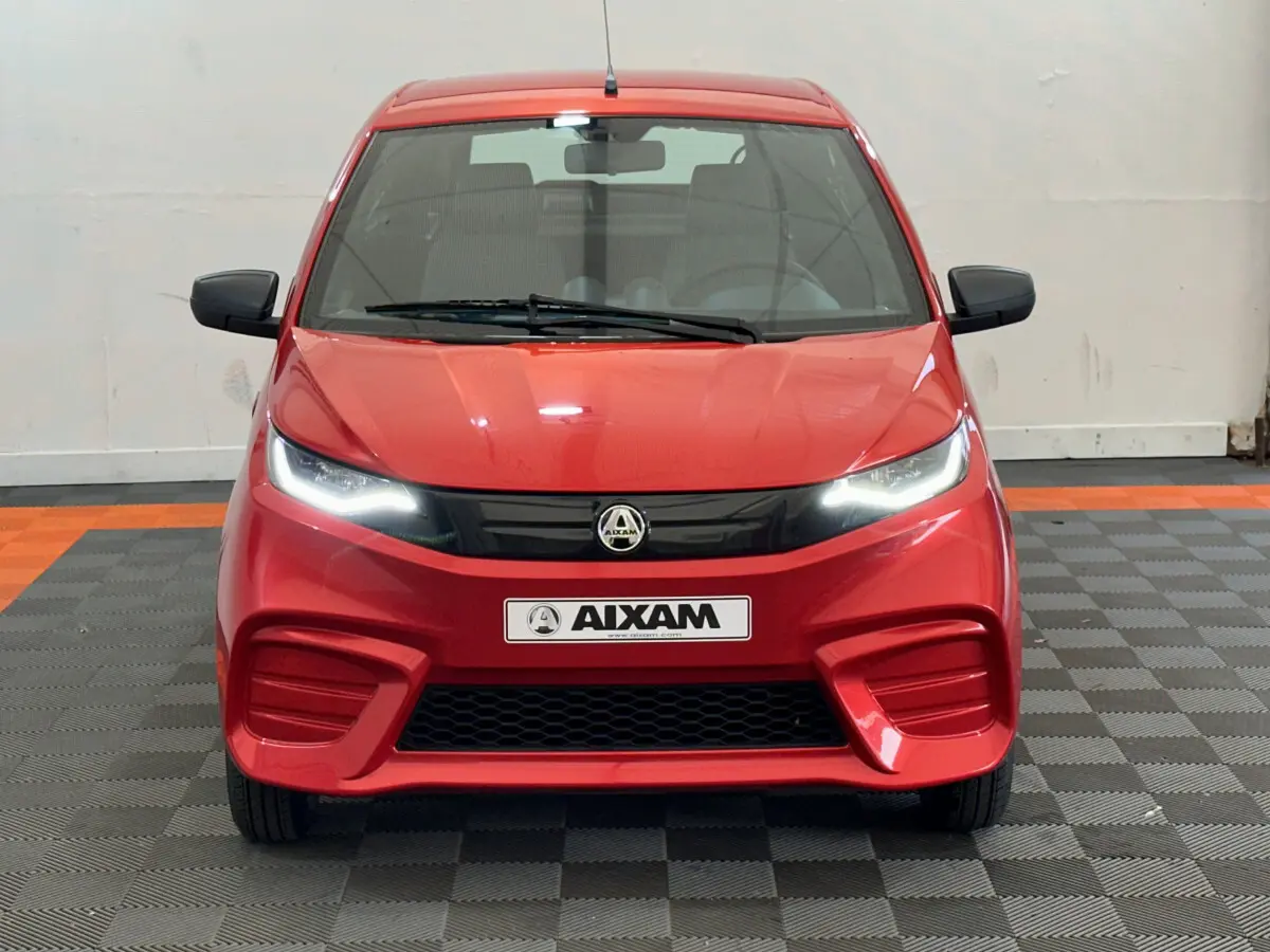 Vue frontale d'une AIXAM AMBITION E CITY PACK rouge 2025 avec phares LED allumés et rétroviseurs noirs.