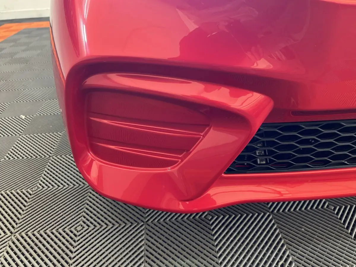 Gros plan sur la partie avant gauche rouge de l'AIXAM AMBITION E CITY PACK 2025 avec prise d'air et grille noire.