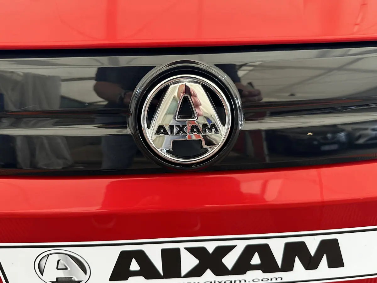 Gros plan sur le logo chromé AIXAM sur la calandre rouge vif de la microcar électrique 2025 Ambition E City Pack.