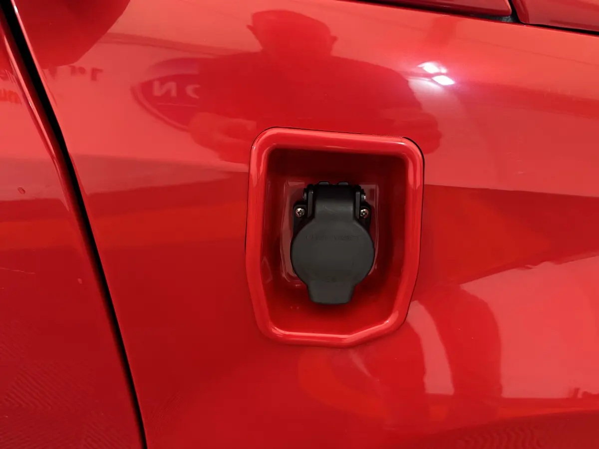 Prise de recharge électrique en gros plan sur la portière rouge côté conducteur de l'Aixam Ambition E City Pack 2025.