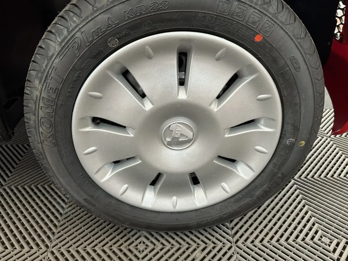 Gros plan sur la roue avant droite d'une Aixam Ambition E City Pack rouge avec enjoliveur argenté et pneu Komemet Plus.