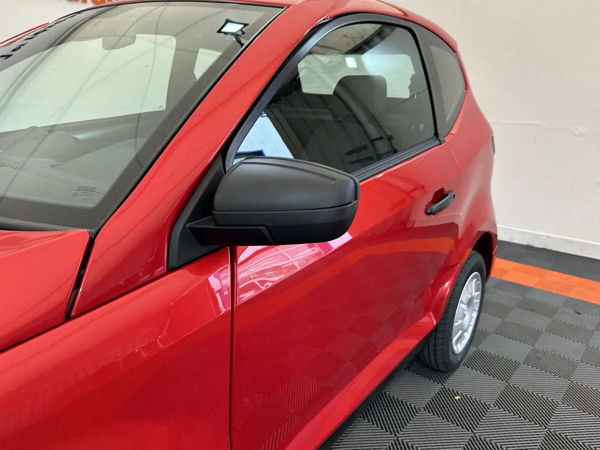 Vue de côté gauche rapprochée sur l'AIXAM AMBITION E CITY PACK rouge 2025 avec rétroviseur caméra visible.