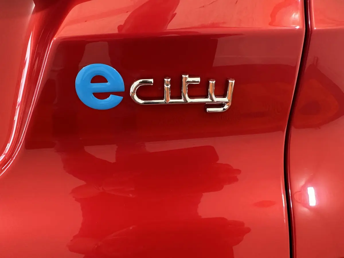 Gros plan sur l’inscription e city en bleu et chrome sur la carrosserie rouge de l’AIXAM AMBITION E CITY PACK 2025 électrique.