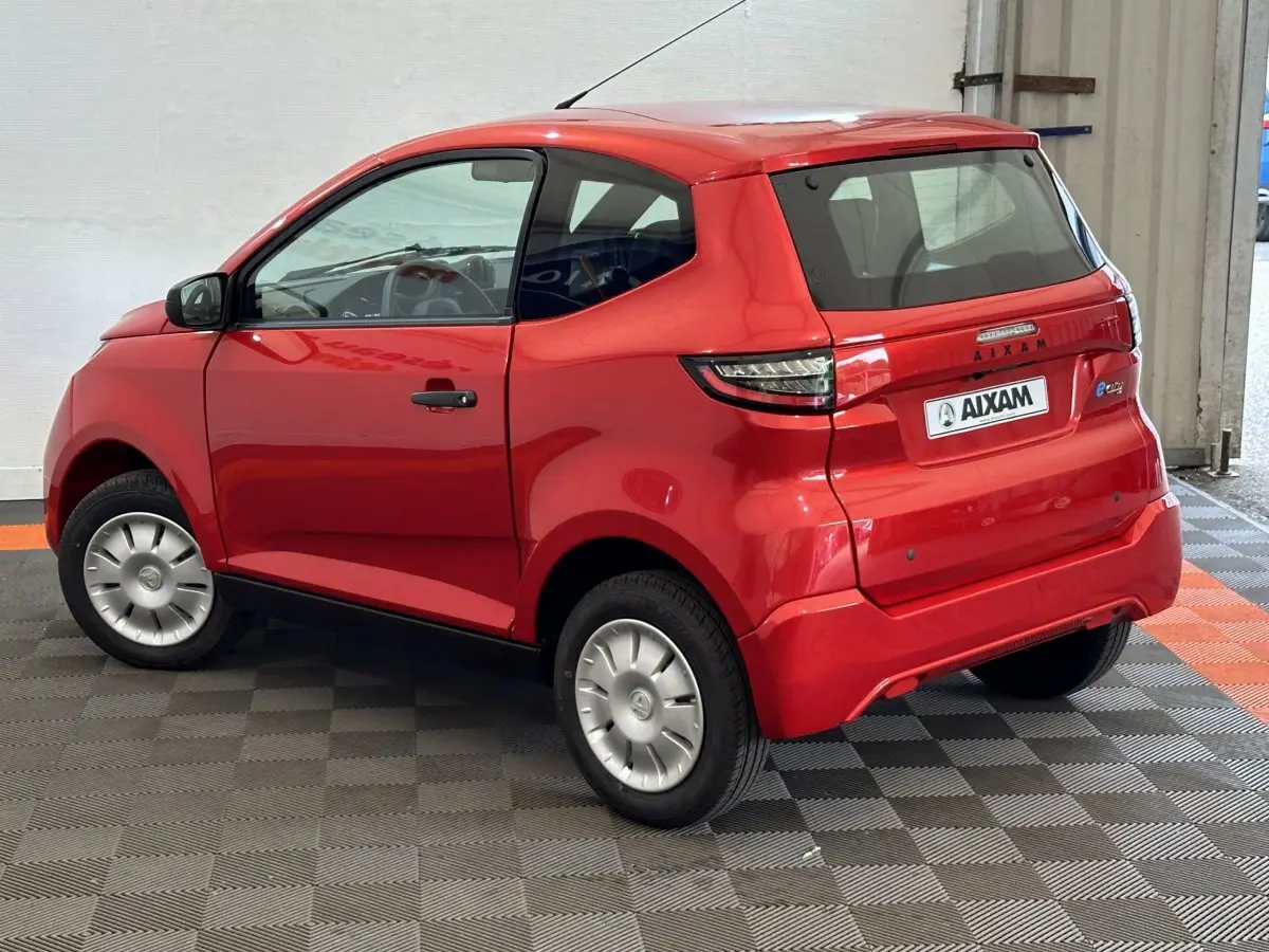 Vue 3/4 arrière droite d'une AIXAM Ambition E City Pack rouge 2025 avec rétroviseur caméra côté conducteur.