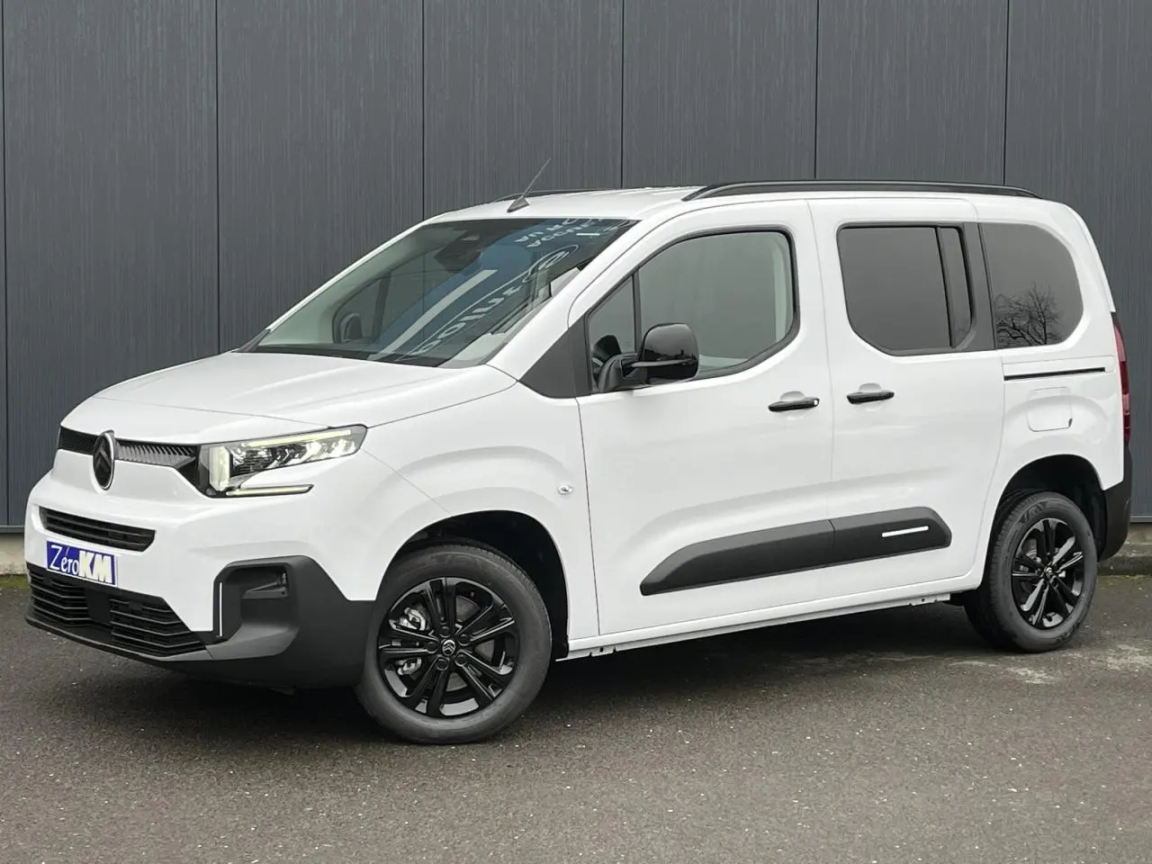 Vue 3/4 avant droit du Citroën Berlingo Multispace blanc Glacier avec jantes alliage noires et barres de toit.