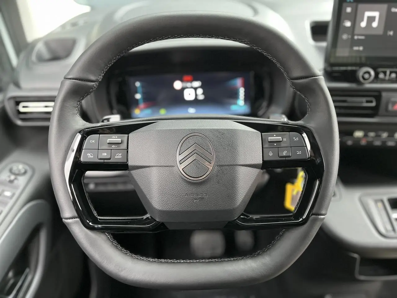 Vue rapprochée du volant cuir multifonctions du Citroën Berlingo blanc glacier avec tableau de bord numérique en arrière-plan.