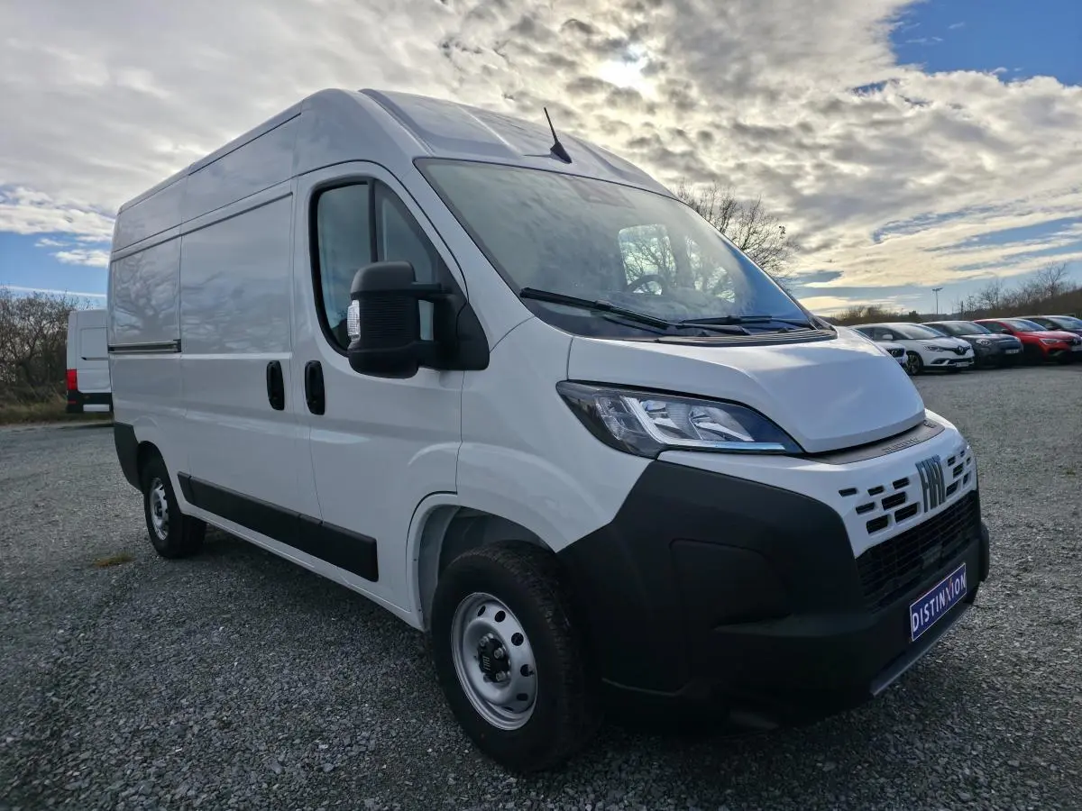 Vue 3/4 avant d'un FIAT Ducato Fourgon blanc avec pare-chocs noirs et roues acier sur parking extérieur.