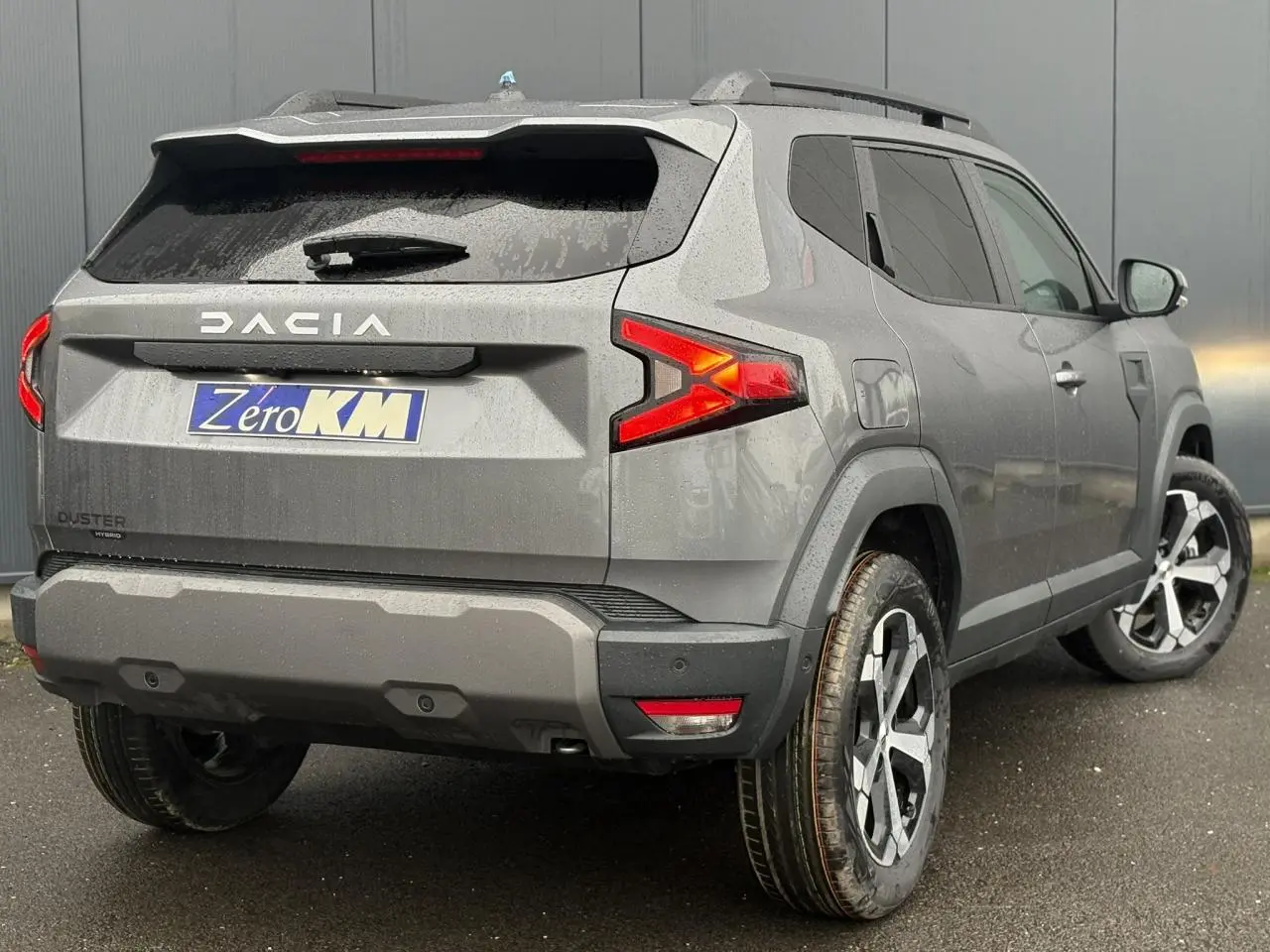 Vue 3/4 arrière droite du Dacia Duster gris schiste avec feux arrière allumés et jantes alliage diamantées.