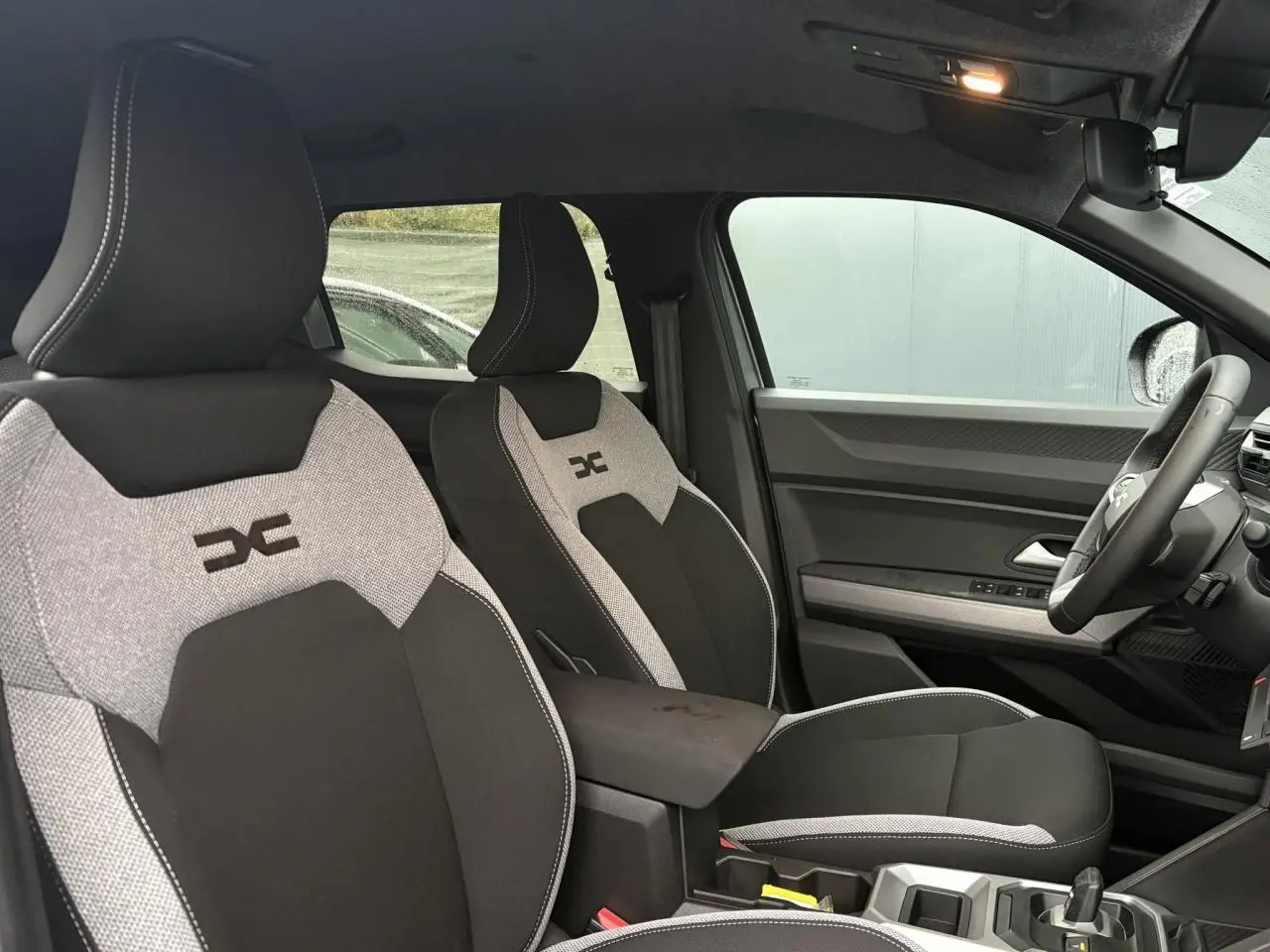 Vue intérieure côté droit montrant les sièges avant gris clair et noir avec logo Duster brodé sur appuie-tête.