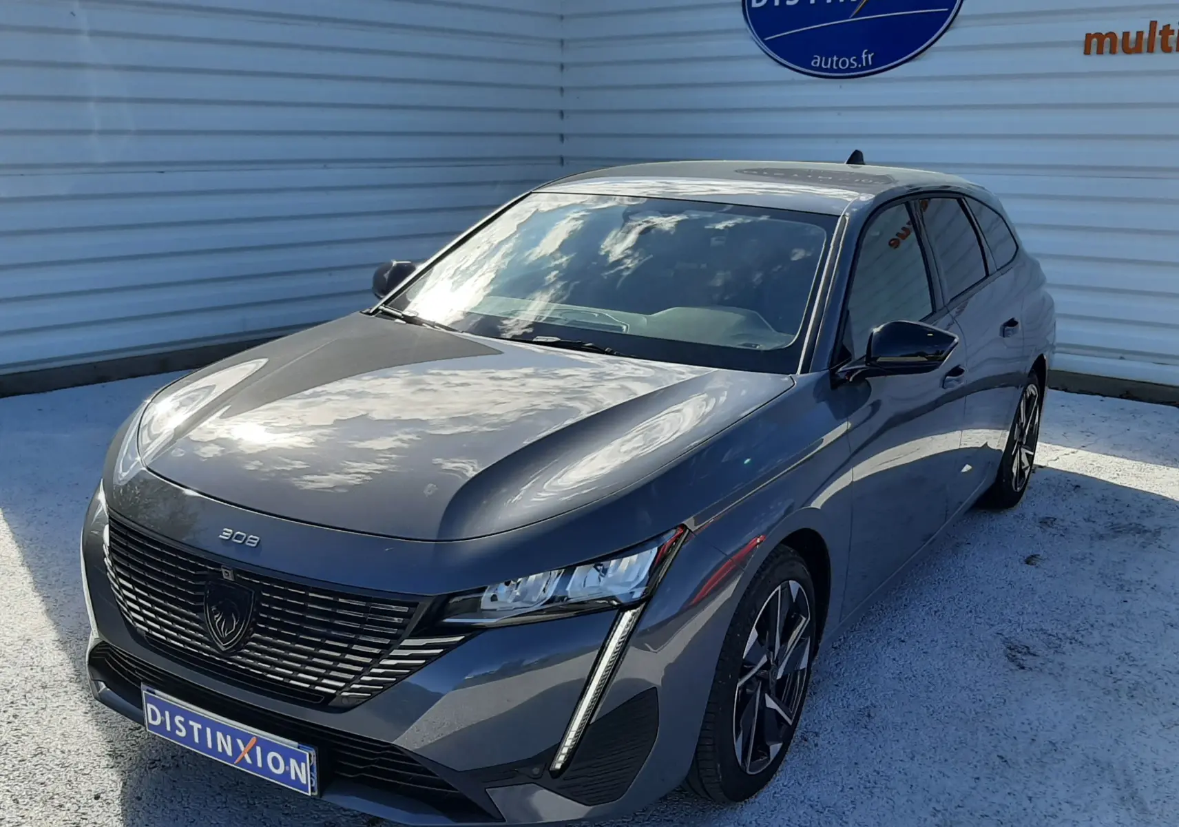 Peugeot 308 SW Hybrid gris sélénium métal vue 3/4 avant droit, avec calandre noire et feux LED verticaux distinctifs.