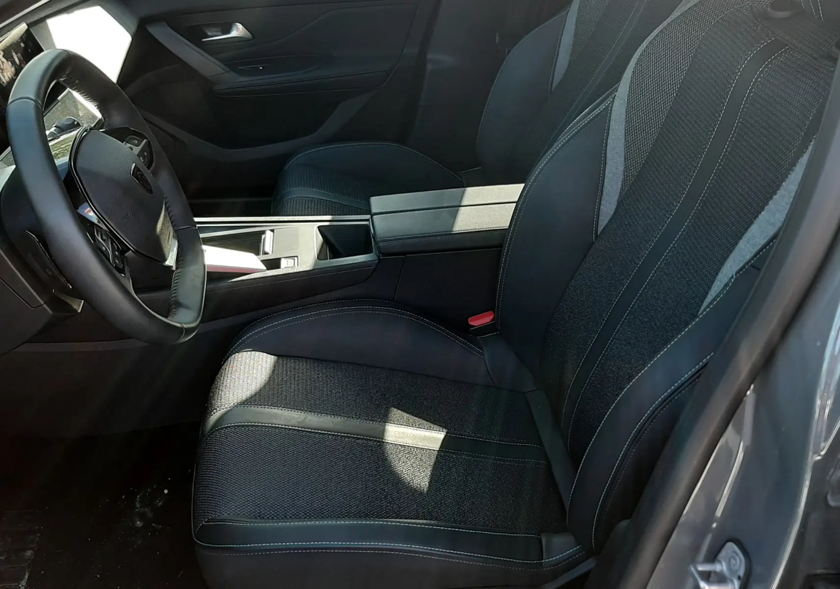 Vue intérieure côté conducteur de la Peugeot 308 SW Hybrid 2025 gris sélénium, sièges tissu et cuir avec surpiqûres blanches.
