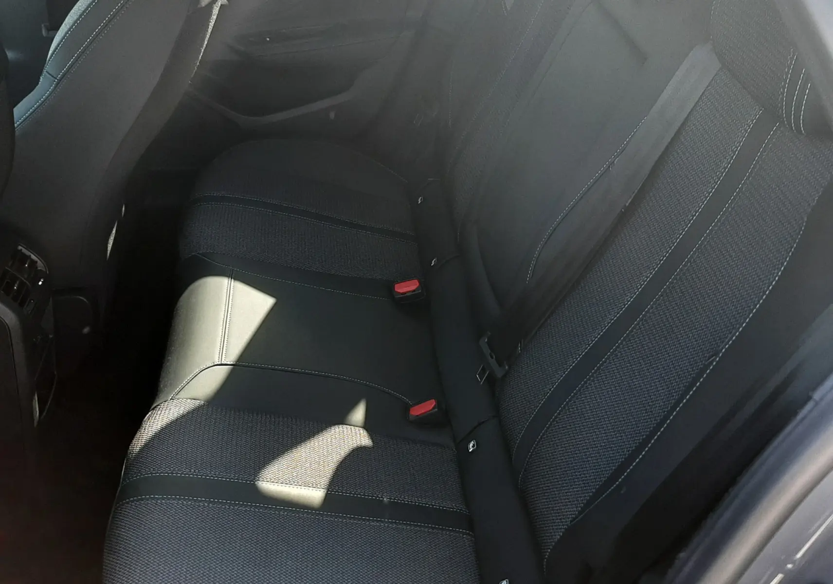 Vue intérieure côté arrière droit montrant la banquette arrière en tissu gris foncé de la Peugeot 308 SW Hybrid 2025.