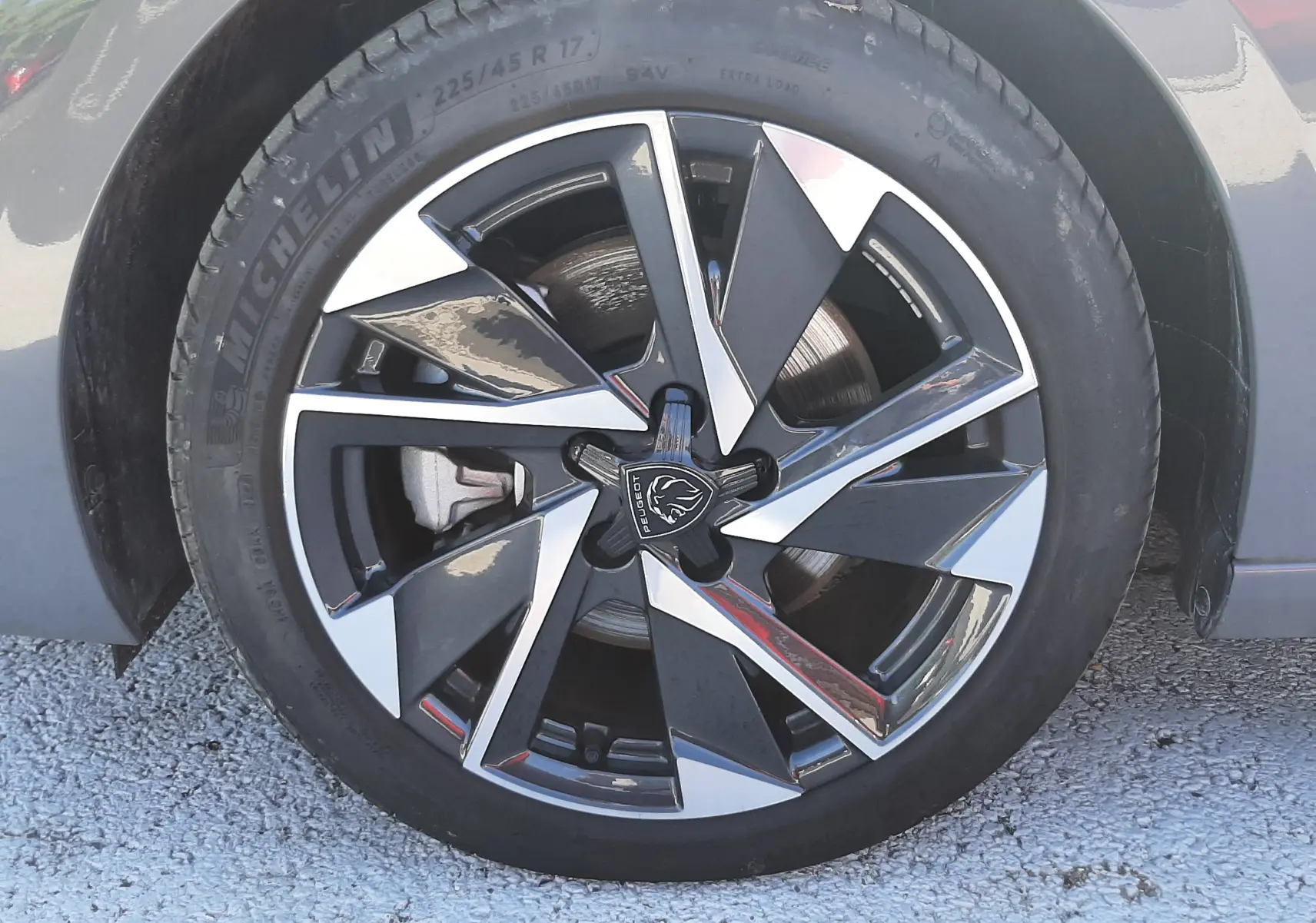 Gros plan sur la roue avant gauche de la Peugeot 308 SW Hybrid 2025 en gris selenium metal, jante alliage bicolore.