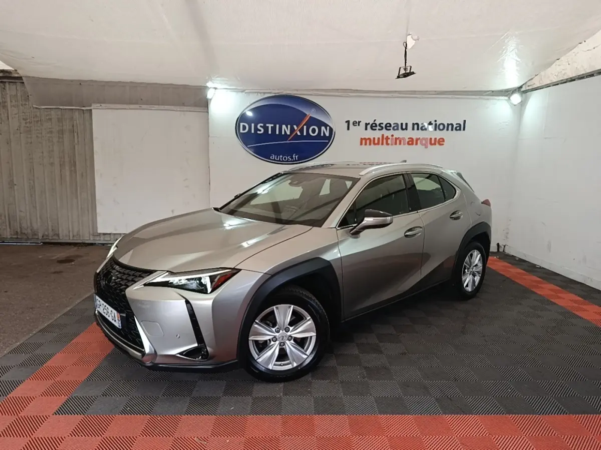 Lexus UX 250H gris clair en 3/4 avant droit, avec jantes alliage et protections noires autour des roues.