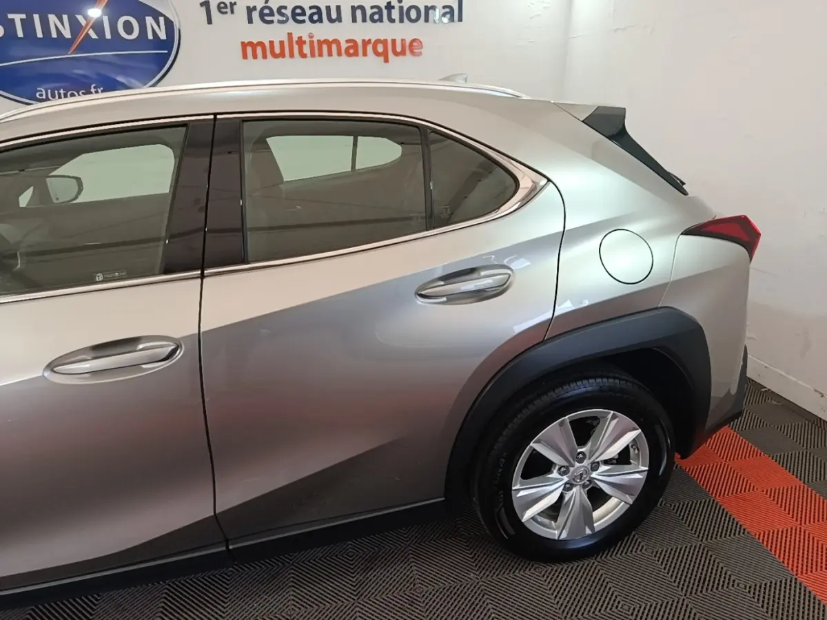 Vue côté droit arrière d’un Lexus UX 250H gris clair avec jante alliage et spoiler de toit visible.