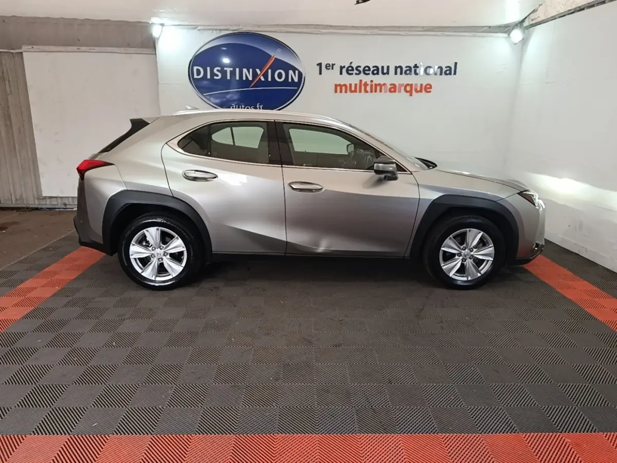 Profil côté gauche d’un Lexus UX 250H gris clair stationné en intérieur avec jantes alliage et protections noires.