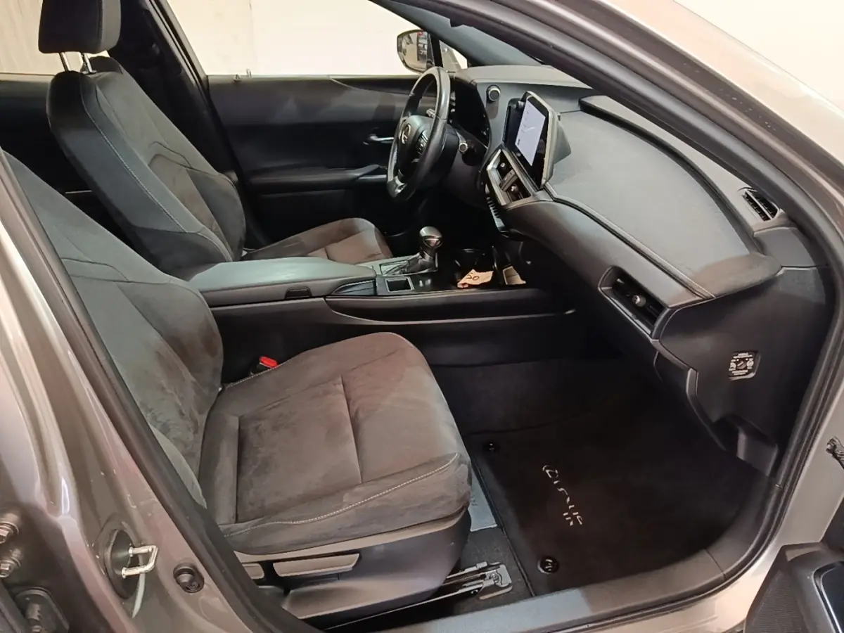 Vue intérieure côté conducteur du Lexus UX 250H gris clair, montrant sièges en tissu et tableau de bord avec écran tactile.