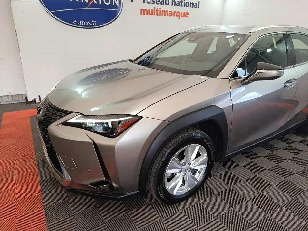 Lexus UX 250H gris clair en 3/4 avant droit, avec calandre noire distinctive et jantes argentées.