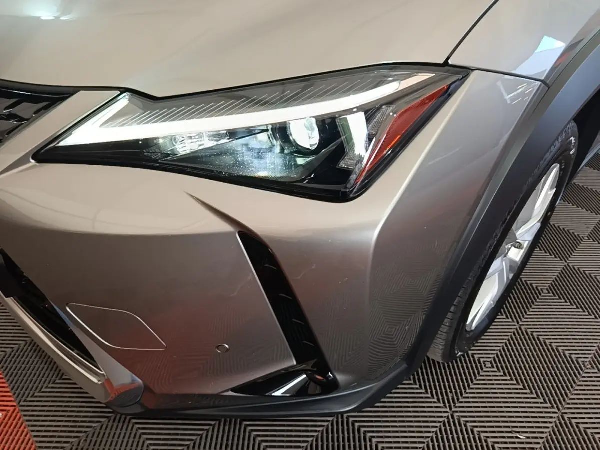 Gros plan sur l’avant droit gris clair du Lexus UX 250H 2WD avec phare LED et partie de la roue visible.