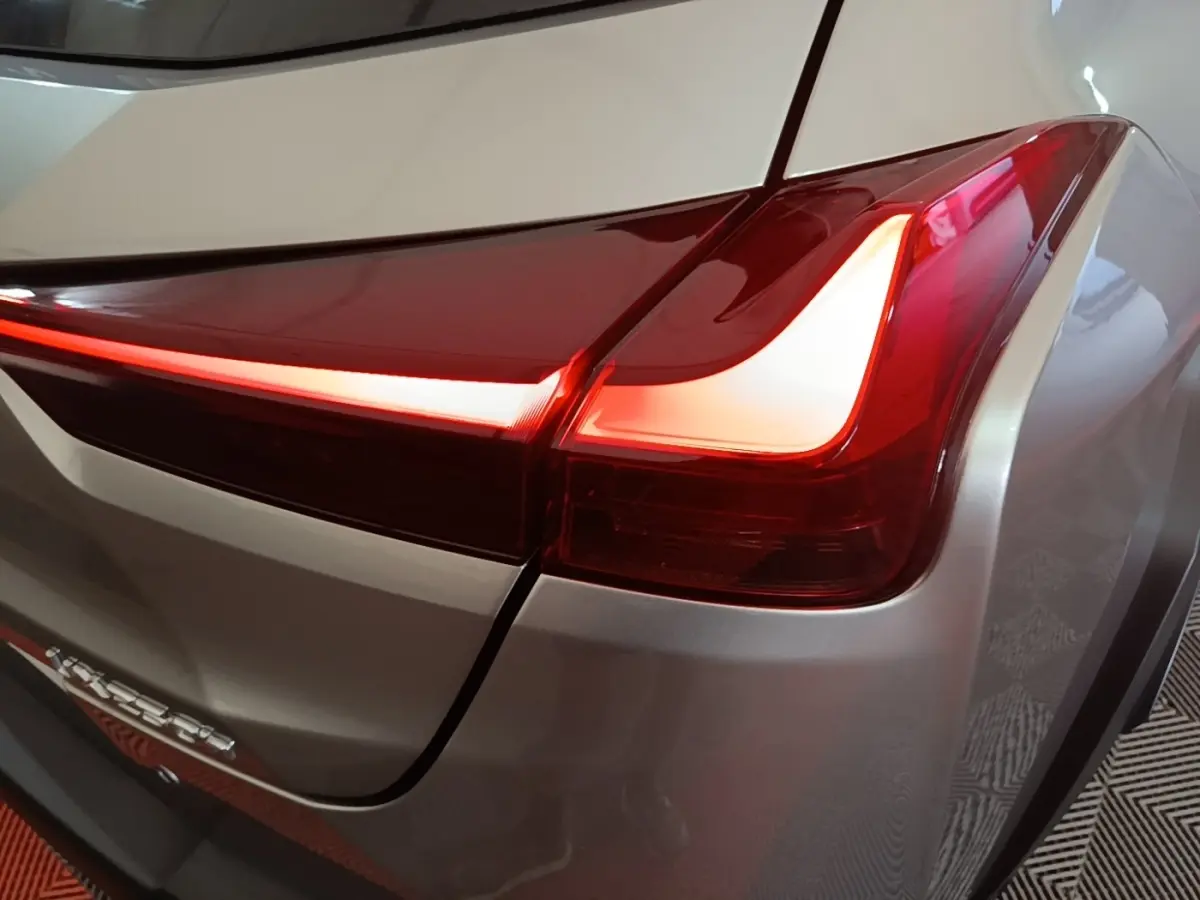 Gros plan sur le feu arrière droit rouge allumé d’un Lexus UX 250H gris clair, avec lignes LED distinctives.