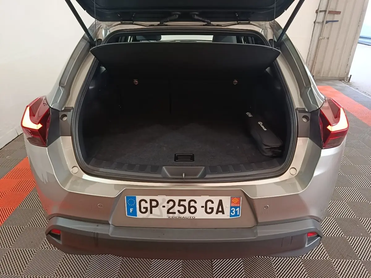 Vue arrière ouverte du coffre d'un Lexus UX 250H gris clair avec feux arrière allumés dans un garage.