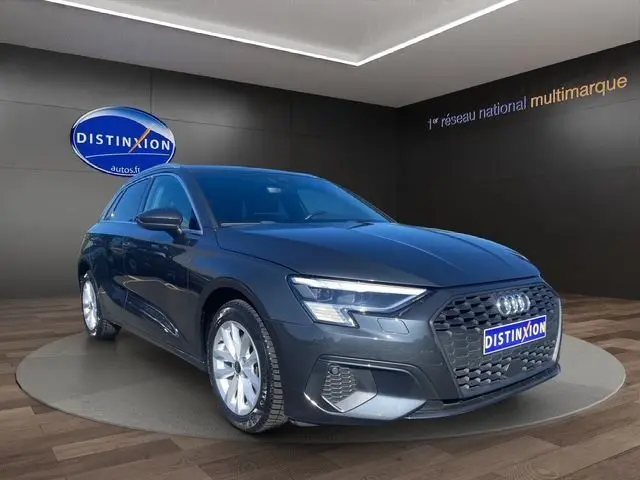 Audi A3 Sportback gris Manhattan en 3/4 avant droit, avec phares à matrice LED et vitres arrière surteintées visibles.