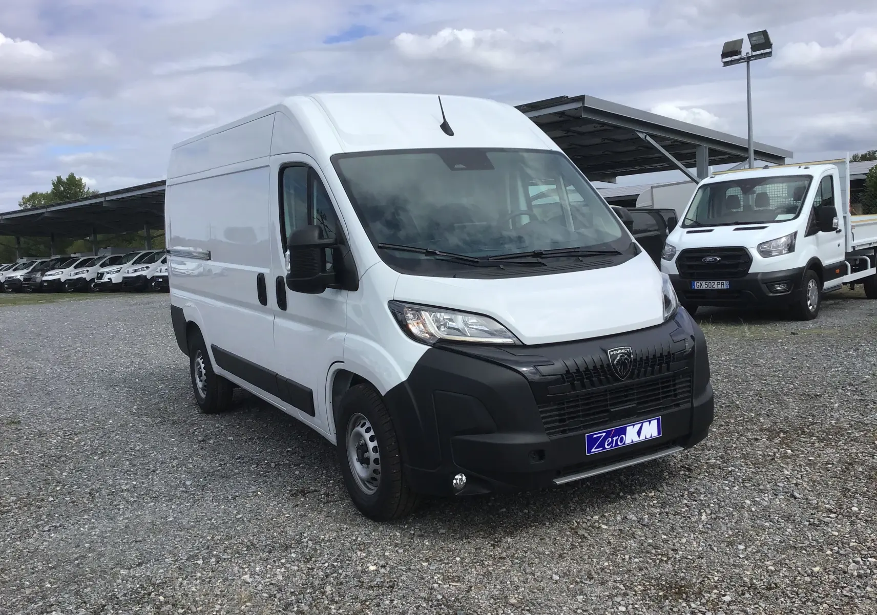 PEUGEOT Boxer Fourgon blanc en vue 3/4 avant droit sur parking avec calandre noire et plaque Zero KM.