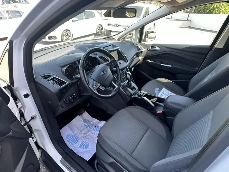 Intérieur du Ford C-MAX blanc 2017, vue côté conducteur ouverte, tableau de bord et sièges gris visibles.