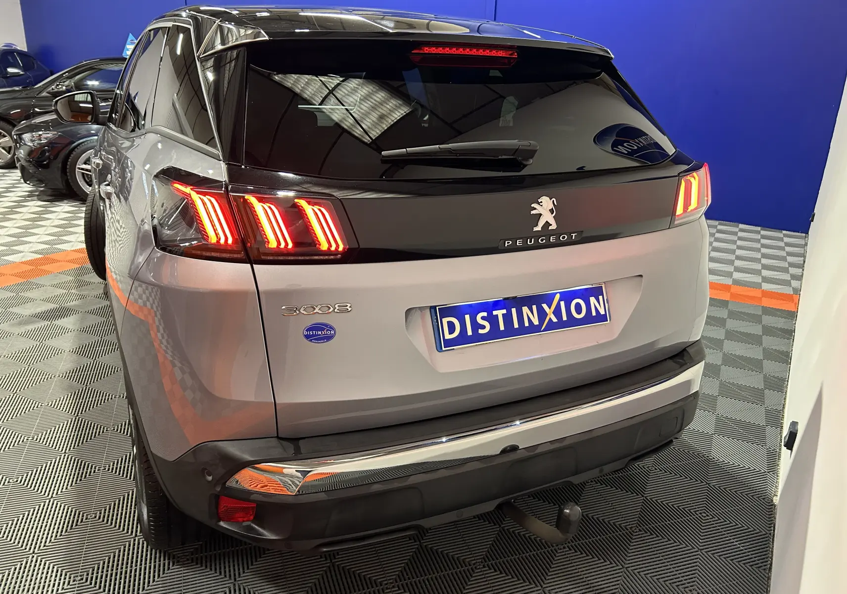 Vue 3/4 arrière d’un Peugeot 3008 gris Artense avec toit noir, feux allumés et attelage visible.