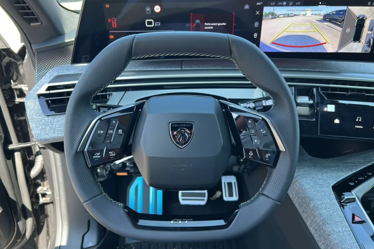 Vue centrée sur le volant cuir multifonctions du Peugeot 3008 New Hybrid GT avec écran digital et affichage caméra 360° en arrière-plan.