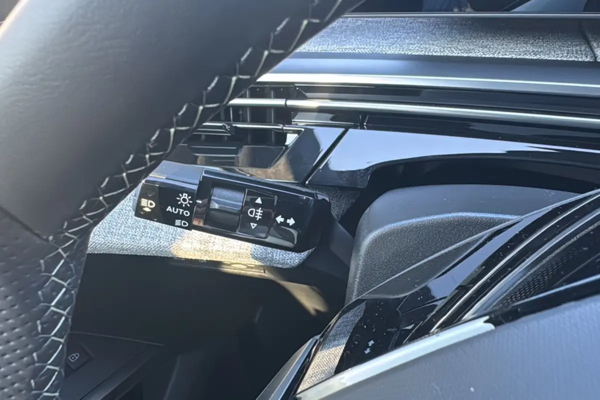 Gros plan sur la commande des feux et clignotants à gauche du volant cuir du Peugeot 3008 New Hybrid 2025.