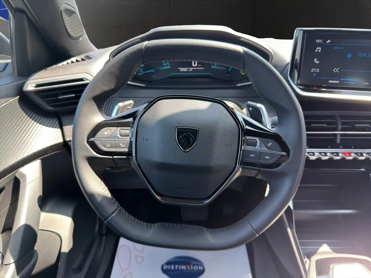 Vue rapprochée du volant cuir multifonctions noir du Peugeot 2008 Hybrid 145 e-DCS6 STYLE avec tableau de bord digital.