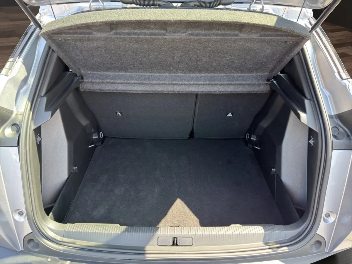 Coffre ouvert vu de l'arrière d'un Peugeot 2008 Hybrid 145 gris clair, montrant un espace de chargement propre et spacieux.