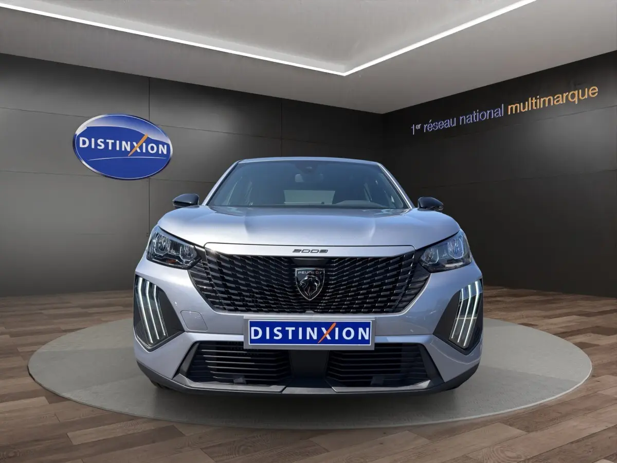 Vue frontale du Peugeot 2008 Hybrid gris clair avec calandre noire et feux LED verticaux allumés.