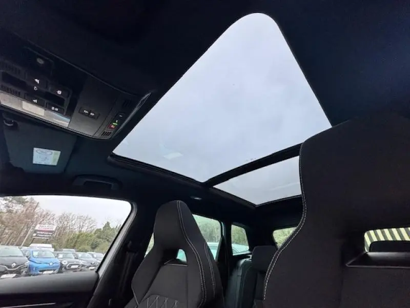 Vue intérieure du toit panoramique en verre du Skoda Karoq gris, avec sièges avant sport noirs et ciel nuageux visible.