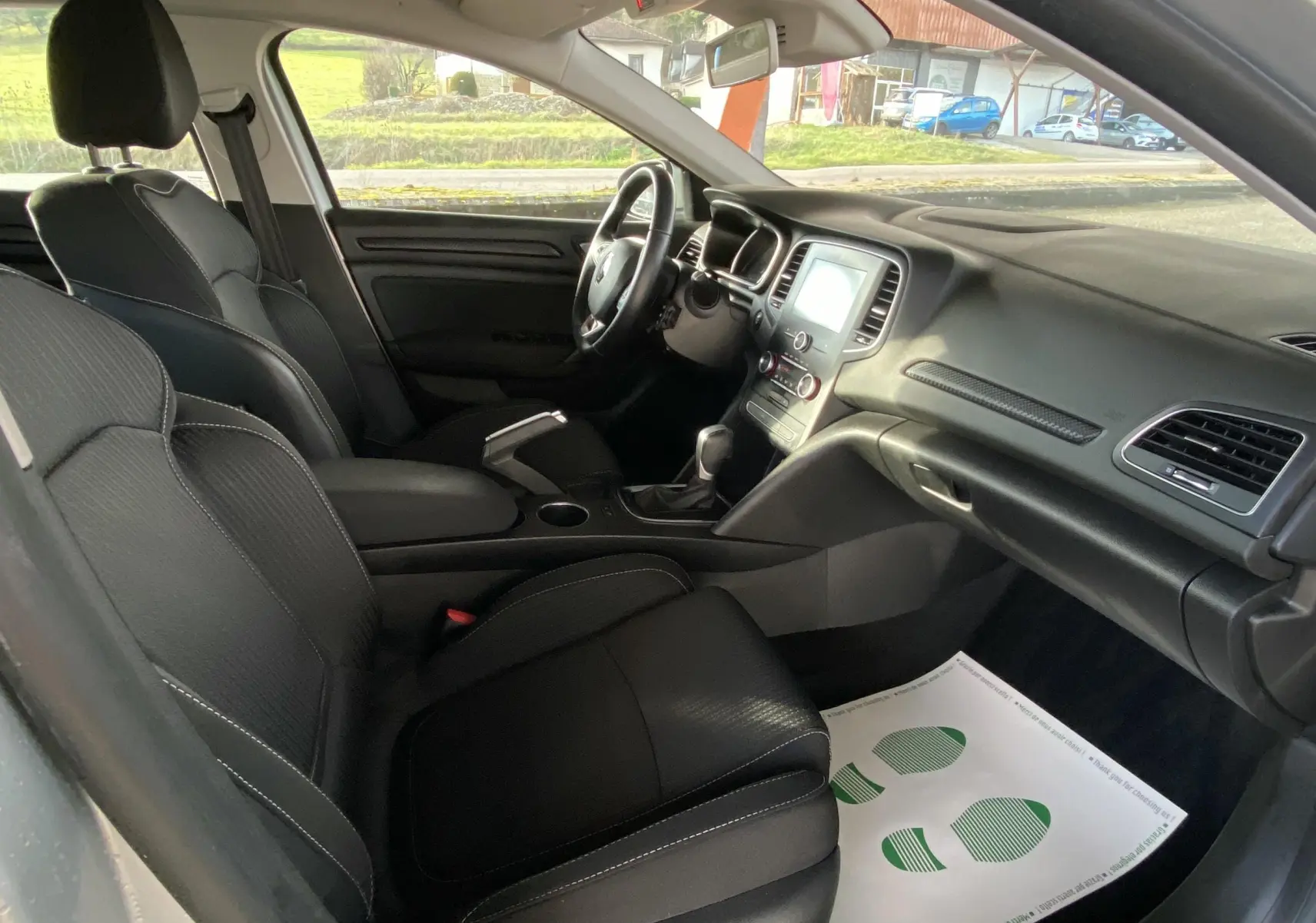 Intérieur noir de la Renault Mégane IV Berline vu côté passager, avec tableau de bord et console centrale visibles.