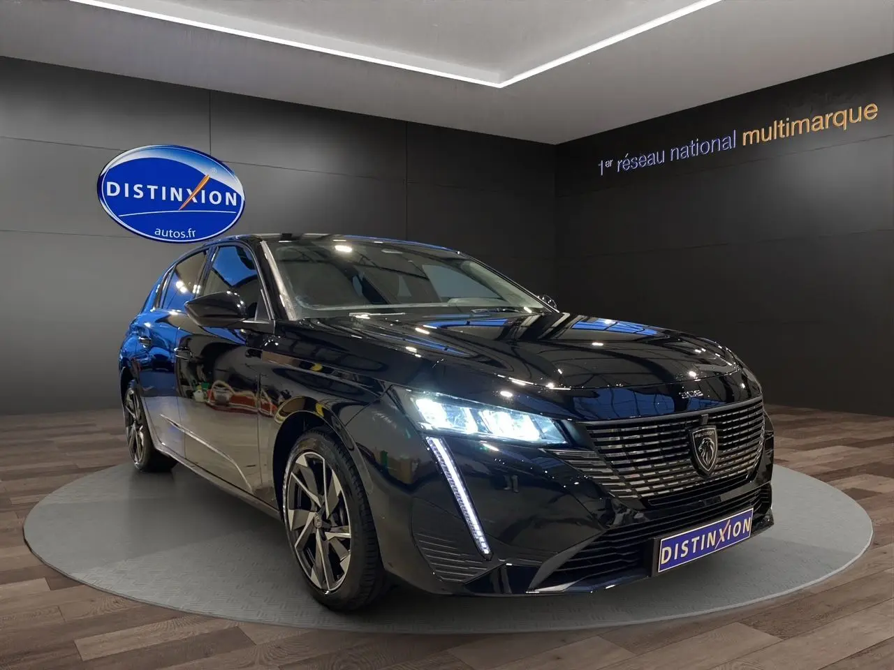 Peugeot 308 noir Perla Nera vue 3/4 avant droit avec phares LED allumés en showroom.