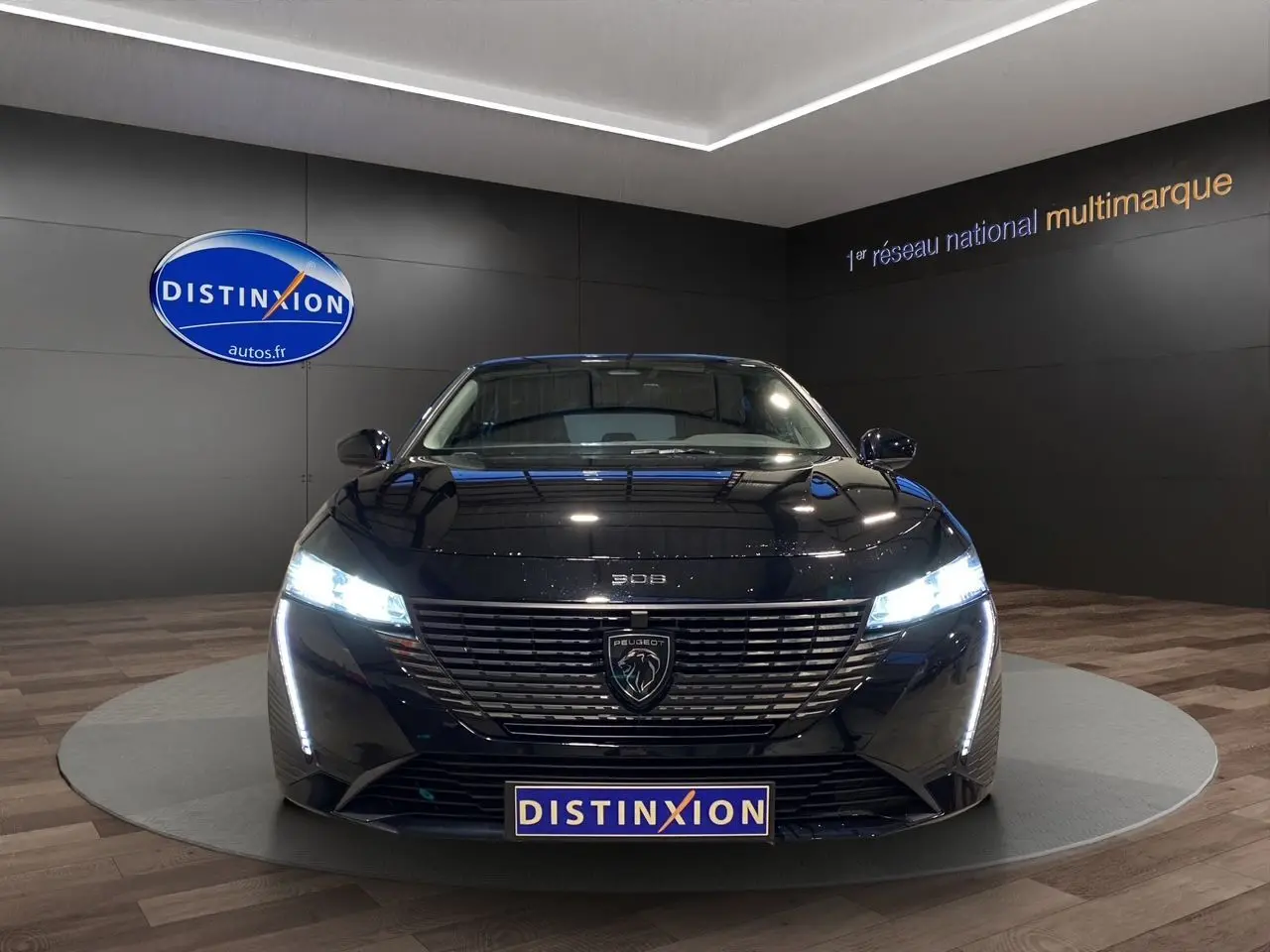 Peugeot 308 1.5 BlueHDi 130 Allure en noir Perla Nera, vue de face avec phares LED allumés dans showroom.