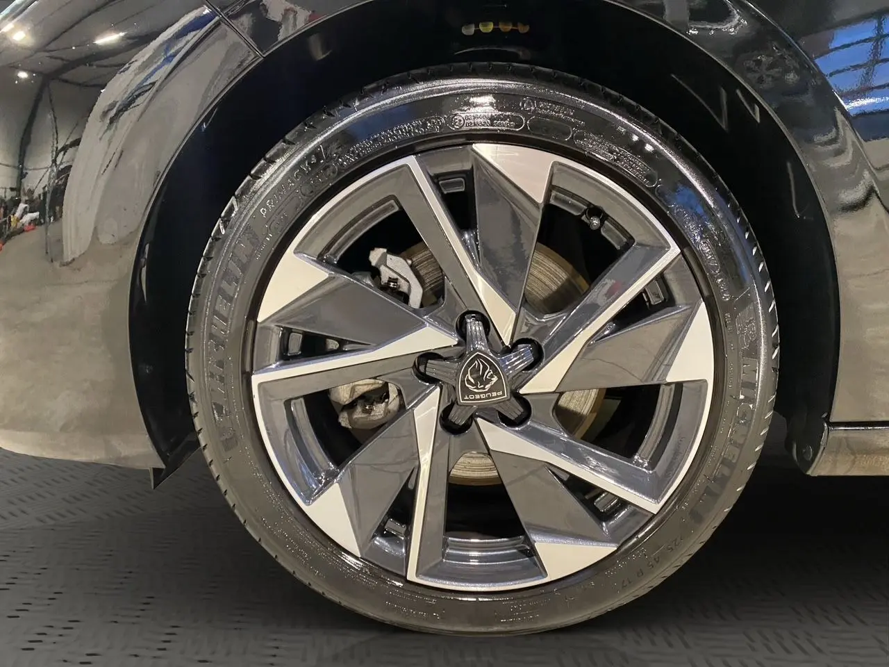 Gros plan sur la roue avant gauche noire perla nera d'une Peugeot 308 1.5 BlueHDi 130 Allure 2024 avec jante alliage distinctive.